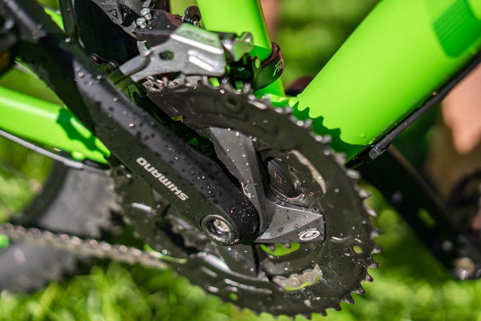 Detailed view of bicycle crankset and gears with water droplets on a green frame.